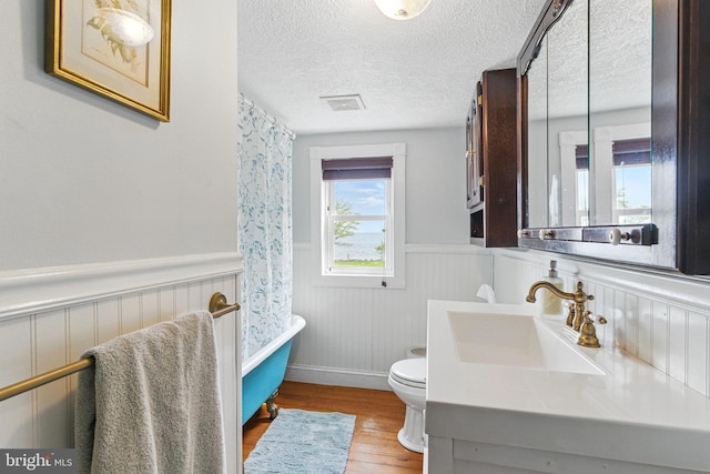 full bathroom with wood finished floors, a bathing tub, wainscoting, toilet, and visible vents
