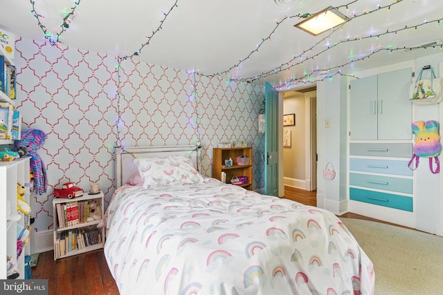 bedroom featuring wood finished floors, wallpapered walls, and baseboards