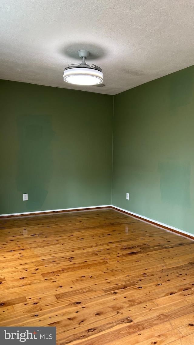 spare room featuring a textured ceiling, wood finished floors, and baseboards