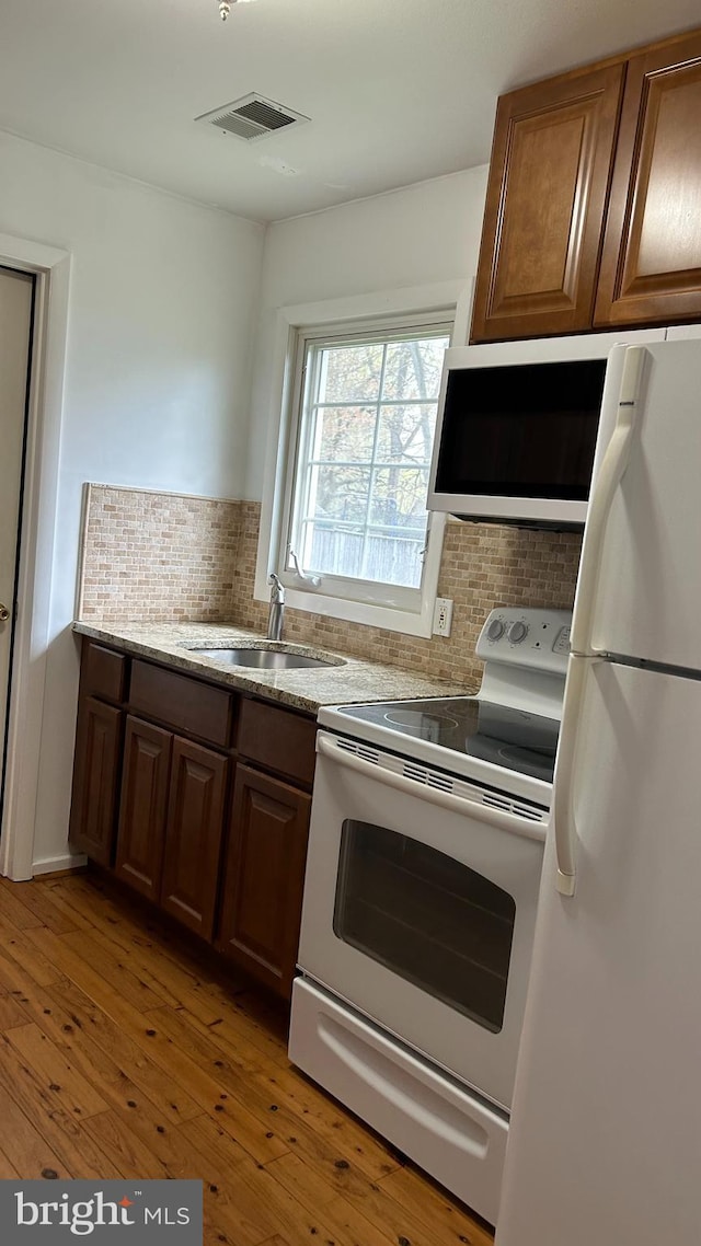 kitchen featuring tasteful backsplash, visible vents, a sink, white appliances, and light wood finished floors