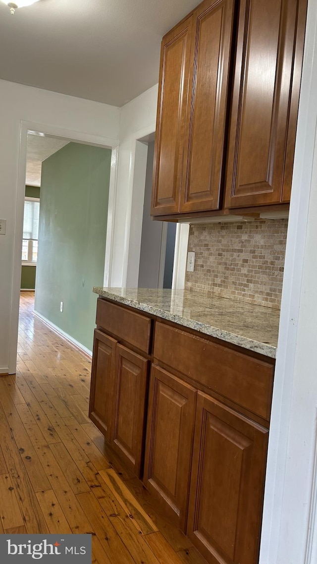 kitchen featuring baseboards, backsplash, light stone countertops, brown cabinets, and light wood finished floors