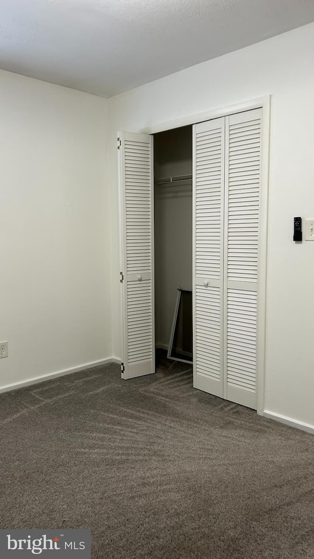 unfurnished bedroom with baseboards, a closet, and dark carpet