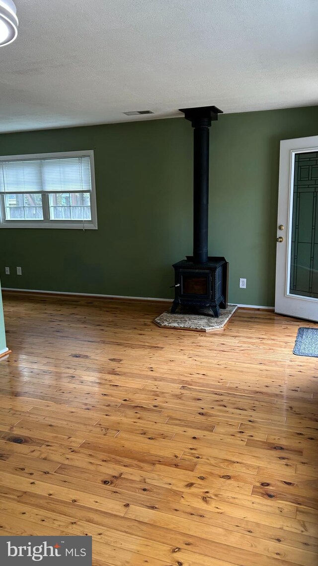 unfurnished living room featuring visible vents, a wood stove, and hardwood / wood-style floors
