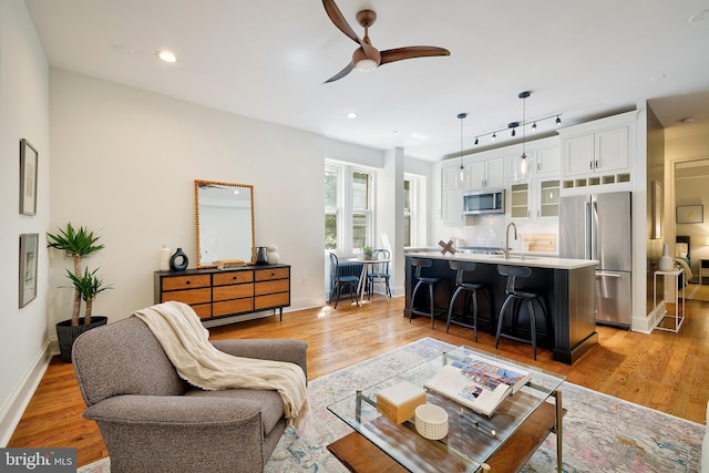 living area featuring a ceiling fan, baseboards, recessed lighting, and light wood-type flooring