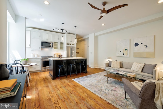 living room featuring light wood-style floors, baseboards, ceiling fan, and recessed lighting