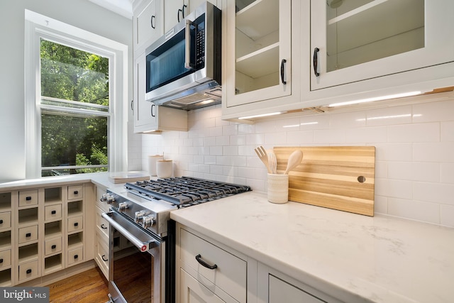 kitchen with glass insert cabinets, light stone counters, tasteful backsplash, and stainless steel appliances