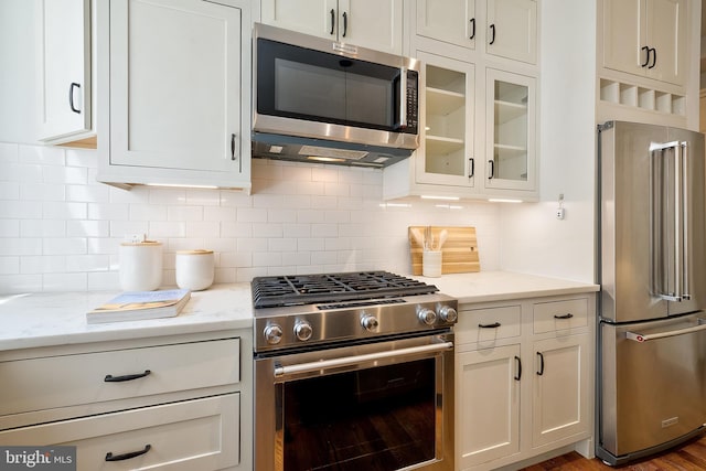 kitchen featuring white cabinets, stainless steel appliances, light stone counters, and glass insert cabinets