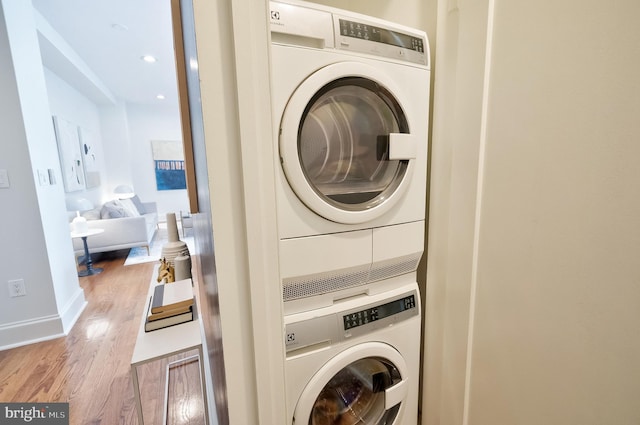 clothes washing area with laundry area, wood finished floors, baseboards, stacked washing maching and dryer, and recessed lighting