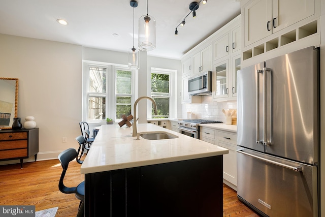 kitchen featuring a sink, a kitchen island with sink, white cabinetry, high end appliances, and glass insert cabinets