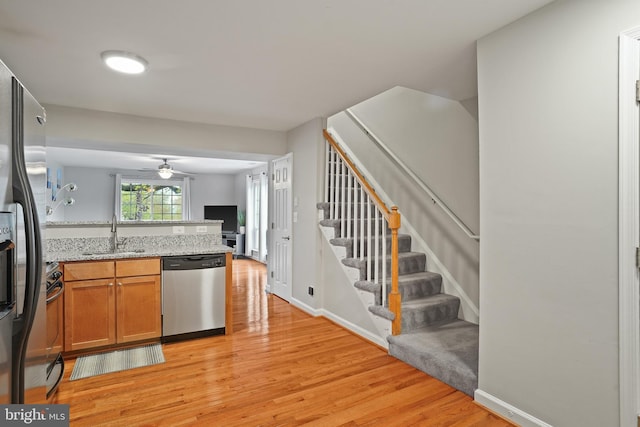 kitchen featuring a peninsula, appliances with stainless steel finishes, a sink, brown cabinets, and light wood finished floors