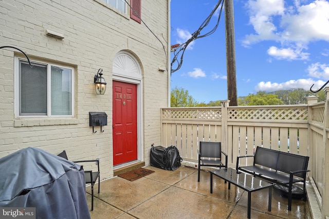 view of exterior entry with a patio area, brick siding, and fence