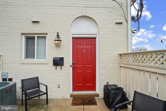 view of exterior entry with brick siding, central AC unit, and fence