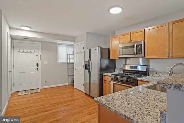 kitchen featuring baseboards, light stone counters, stainless steel appliances, light wood finished floors, and a sink