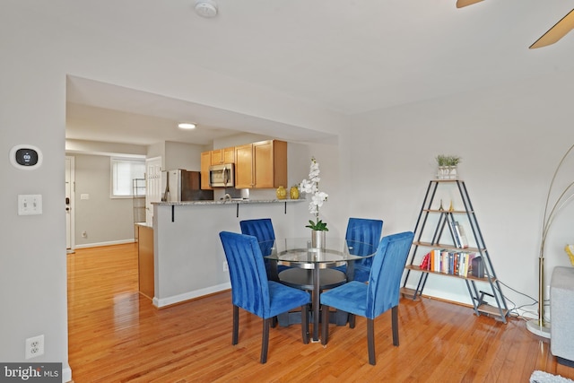 dining space with baseboards, light wood-type flooring, and a ceiling fan