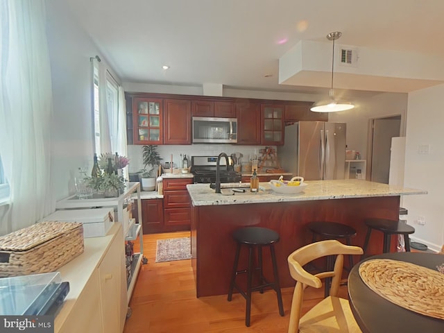 2710 N 47th St, Philadelphia, PA 19131 - kitchen featuring stainless steel appliances, a breakfast bar area, light wood finished floors, decorative light fixtures, and reddish brown cabinets
