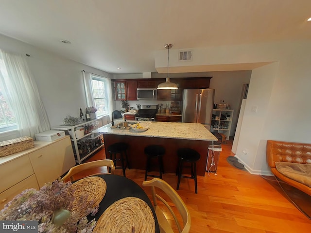 2710 N 47th St, Philadelphia, PA 19131 - kitchen featuring stainless steel appliances, light wood finished floors, a breakfast bar area, hanging light fixtures, and light stone counters