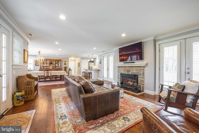 living area with dark wood-type flooring, a fireplace, ornamental molding, and a notable chandelier