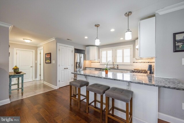 kitchen featuring light stone countertops, a peninsula, stainless steel fridge, and decorative backsplash