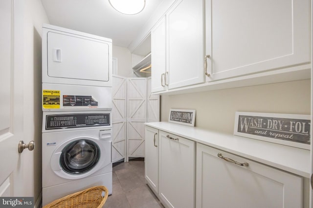 clothes washing area featuring stacked washing maching and dryer, light tile patterned flooring, and cabinet space