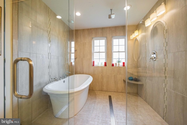 bathroom featuring a tile shower, a freestanding bath, and tile walls