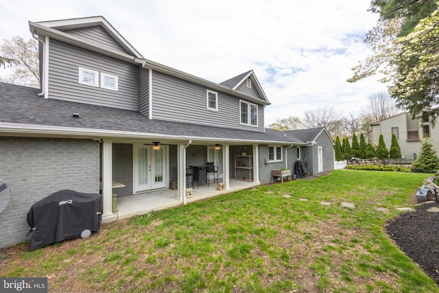 rear view of property featuring a shingled roof, a patio area, ceiling fan, a lawn, and brick siding