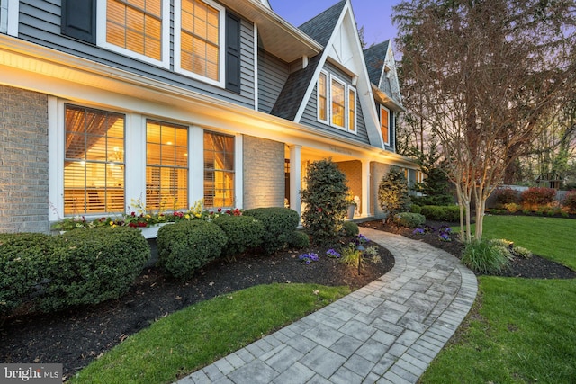 view of side of property featuring a lawn, brick siding, and a shingled roof