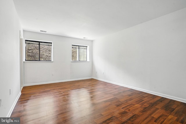 spare room featuring baseboards, visible vents, and wood finished floors
