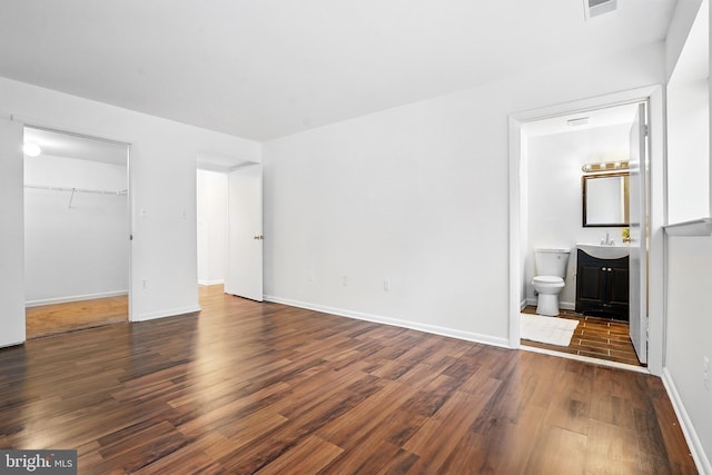 unfurnished bedroom with baseboards, a walk in closet, wood finished floors, and a sink