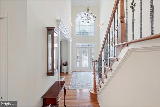 foyer entrance featuring a high ceiling, a notable chandelier, wood finished floors, ornamental molding, and stairway
