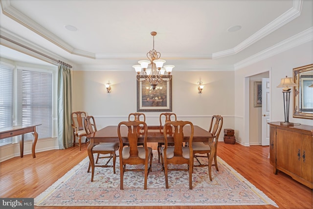 dining area with an inviting chandelier, ornamental molding, baseboards, a tray ceiling, and light wood-style flooring