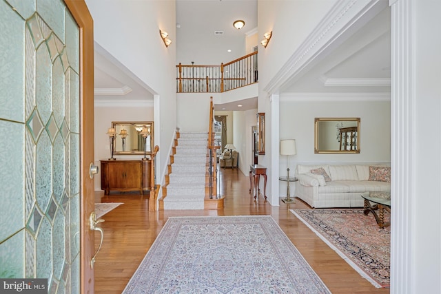 foyer featuring ornamental molding, a towering ceiling, wood finished floors, and stairway