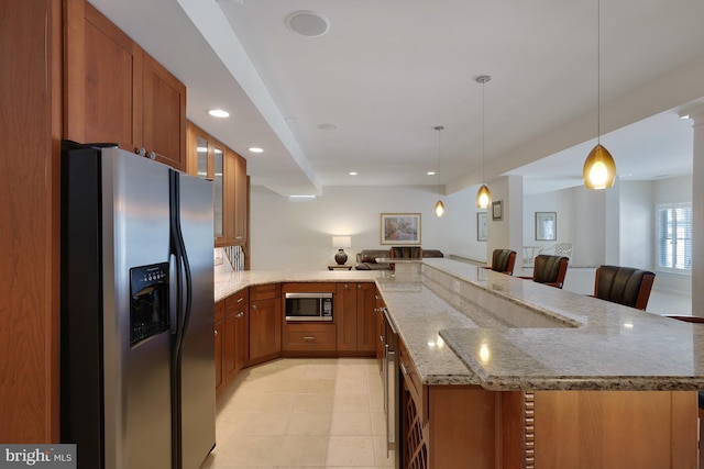kitchen featuring brown cabinets, light stone counters, stainless steel appliances, open floor plan, and a peninsula