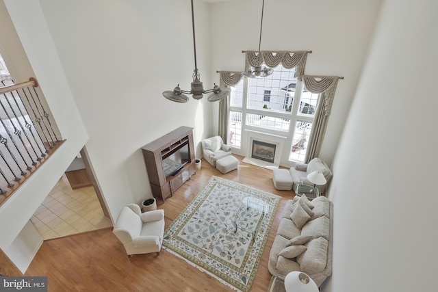 living room with an inviting chandelier, a towering ceiling, a glass covered fireplace, wood finished floors, and stairway