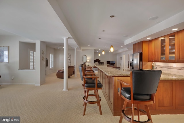 kitchen with brown cabinetry, light stone countertops, glass insert cabinets, open floor plan, and fridge with ice dispenser