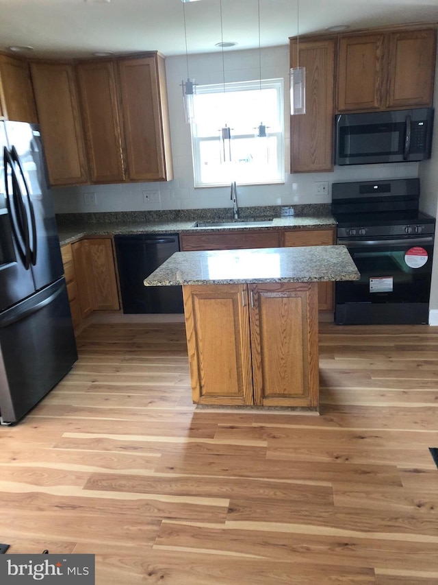 kitchen with a kitchen island, dark stone countertops, a sink, light wood-style floors, and black appliances