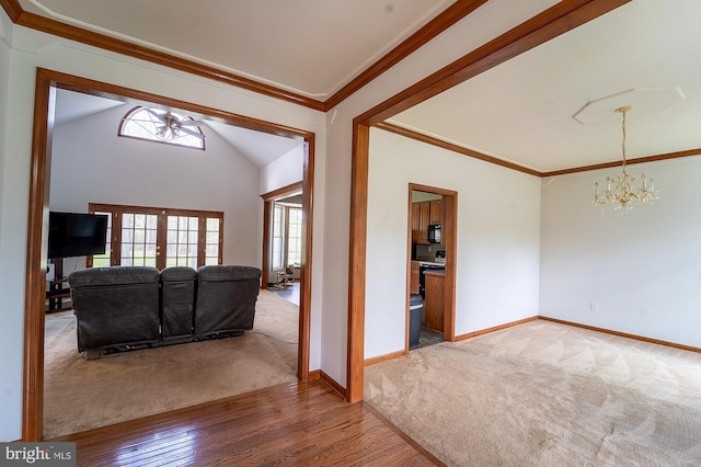 carpeted living area with ceiling fan with notable chandelier, wood finished floors, baseboards, and ornamental molding