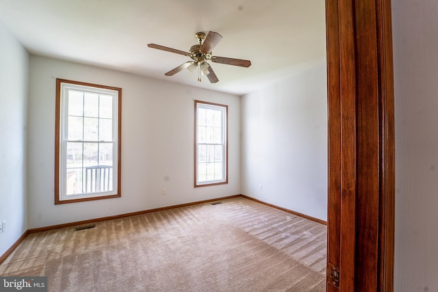 carpeted empty room with baseboards, a ceiling fan, and visible vents