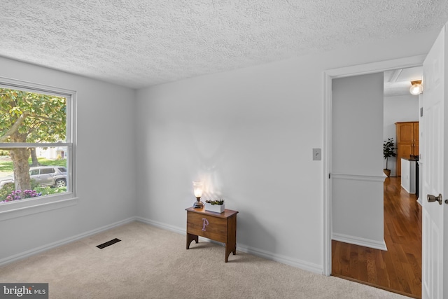 carpeted spare room featuring baseboards, a textured ceiling, and visible vents