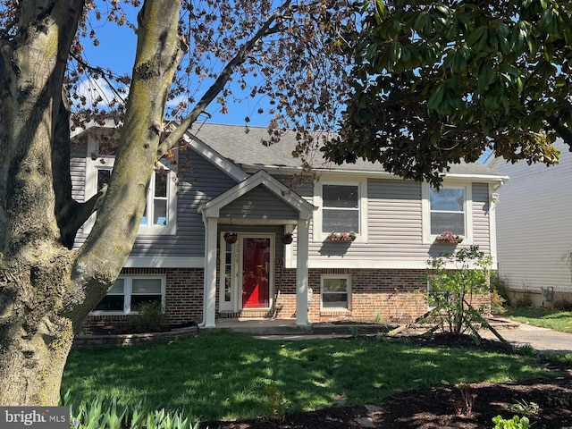 split foyer home featuring a shingled roof, a front lawn, and brick siding