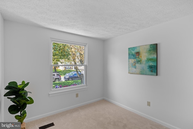 carpeted spare room featuring a textured ceiling, visible vents, and baseboards