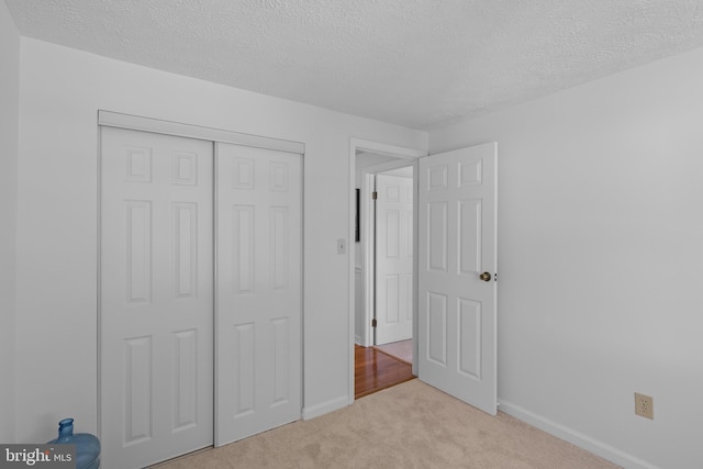 unfurnished bedroom featuring a closet, a textured ceiling, baseboards, and light carpet