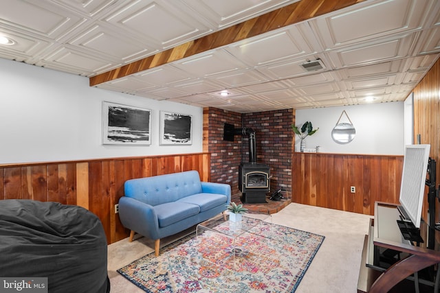 carpeted living area with wainscoting, wooden walls, visible vents, and a wood stove