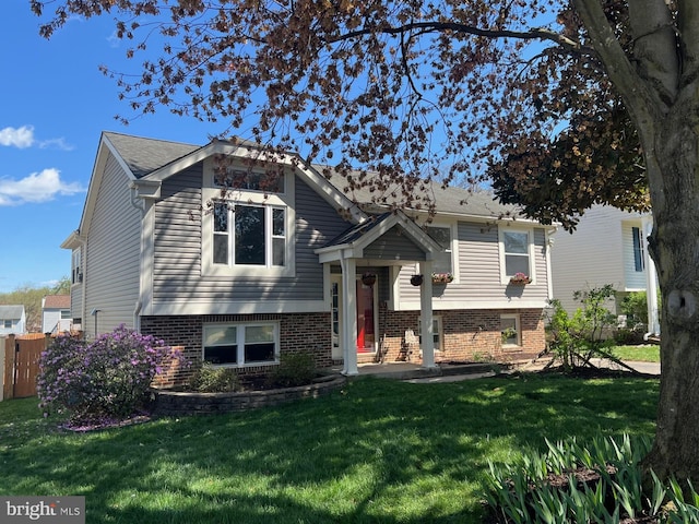 raised ranch with fence, a front lawn, and brick siding