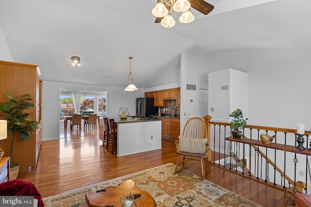 living room featuring ceiling fan, vaulted ceiling, wood finished floors, and visible vents