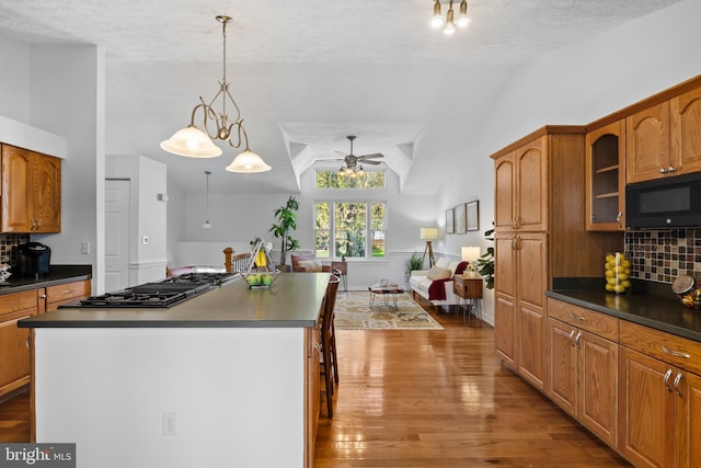 kitchen featuring dark countertops, vaulted ceiling, stainless steel gas stovetop, ceiling fan, and black microwave