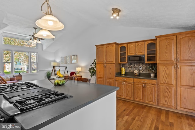 kitchen with dark countertops, vaulted ceiling, brown cabinetry, and glass insert cabinets