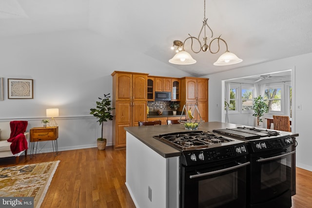 kitchen with brown cabinets, vaulted ceiling, black gas stove, and light wood finished floors