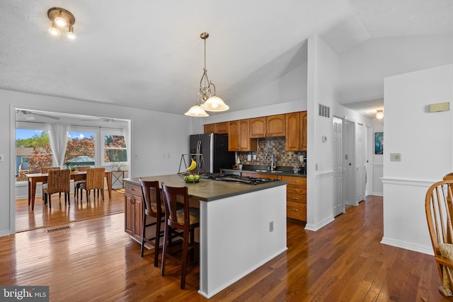 kitchen featuring vaulted ceiling, dark countertops, a sink, stainless steel fridge, and visible vents