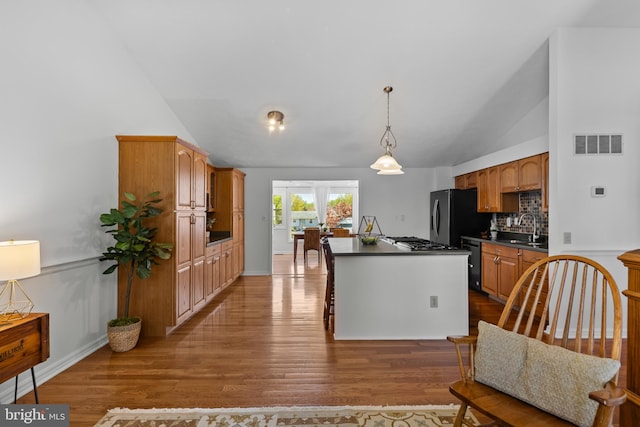 kitchen with a center island, dark countertops, stainless steel fridge with ice dispenser, lofted ceiling, and visible vents