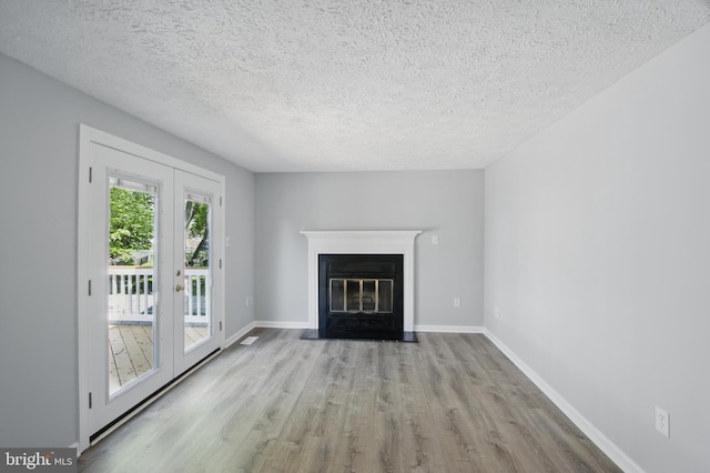 5694 Singletree Dr, Frederick, MD 21703 - unfurnished living room featuring a textured ceiling, wood finished floors, french doors, a fireplace with flush hearth, and baseboards